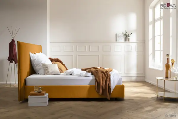 Modernes Schlafzimmer mit gelbem Polsterbett, weißer Bettwäsche am Fenster